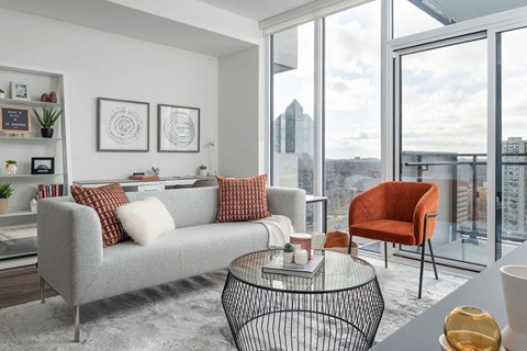 A grey couch with red pillows sits in a modern living room with a view of the city.
