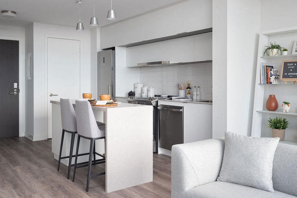 A modern kitchen with a bar stool and a grey couch.