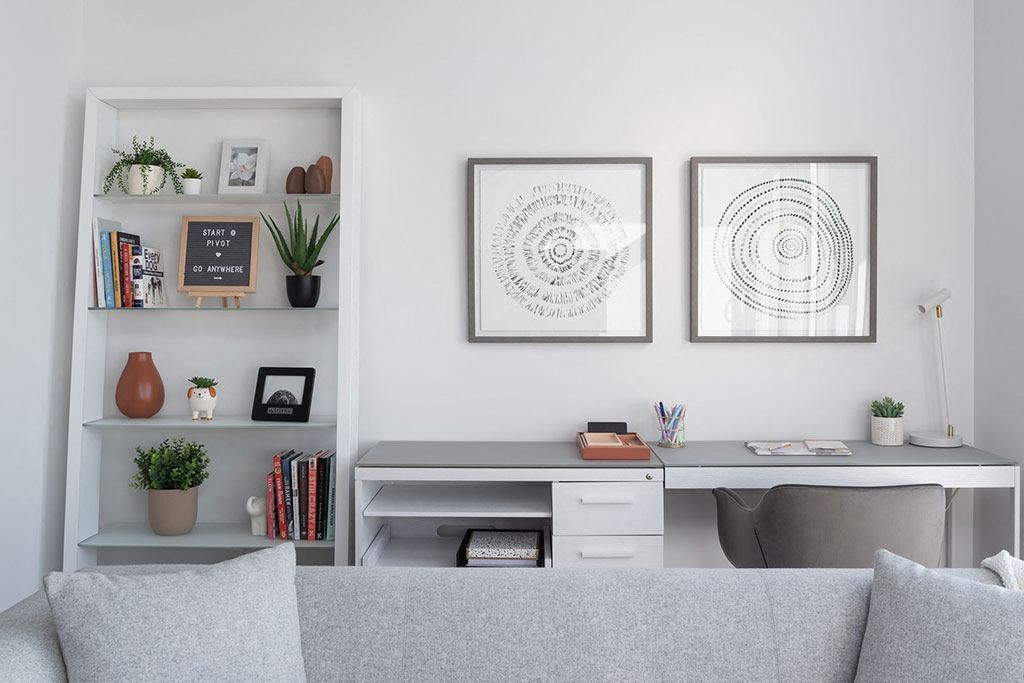 A living room with a grey couch, a white desk, and two framed artworks on the wall.