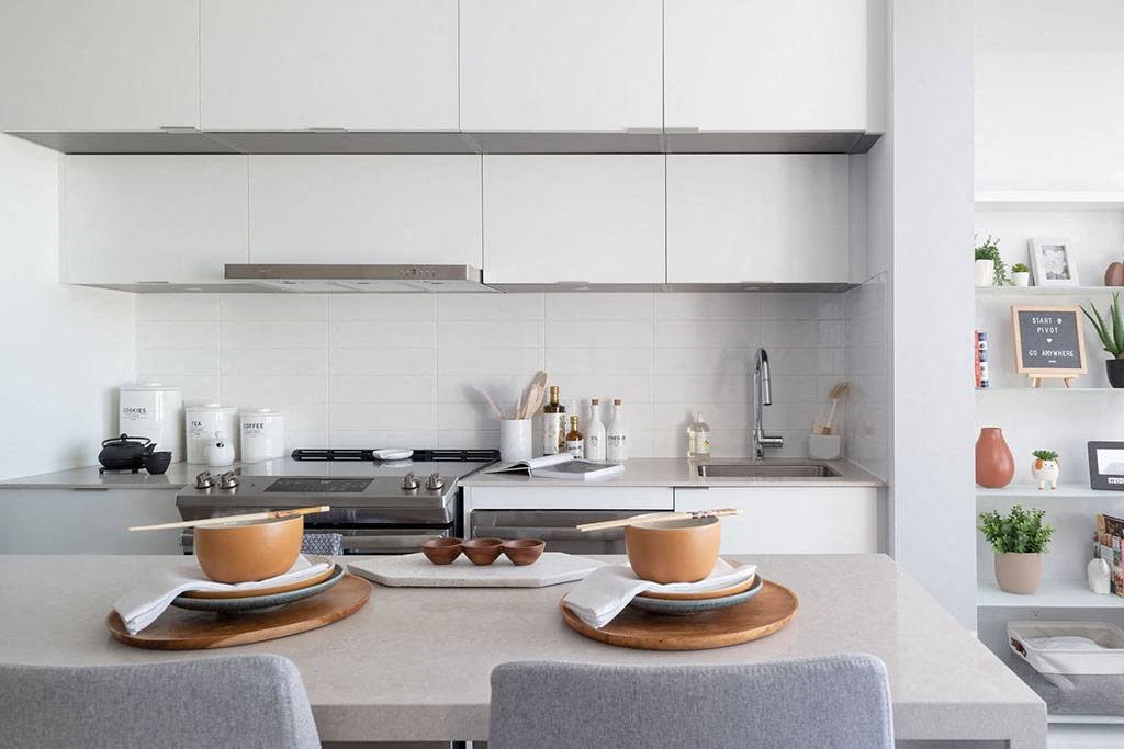 A modern kitchen with a white countertop and grey chairs.
