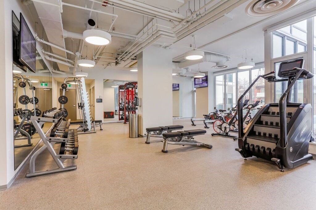 a gym with weights and other exercise equipment in a building with large windows