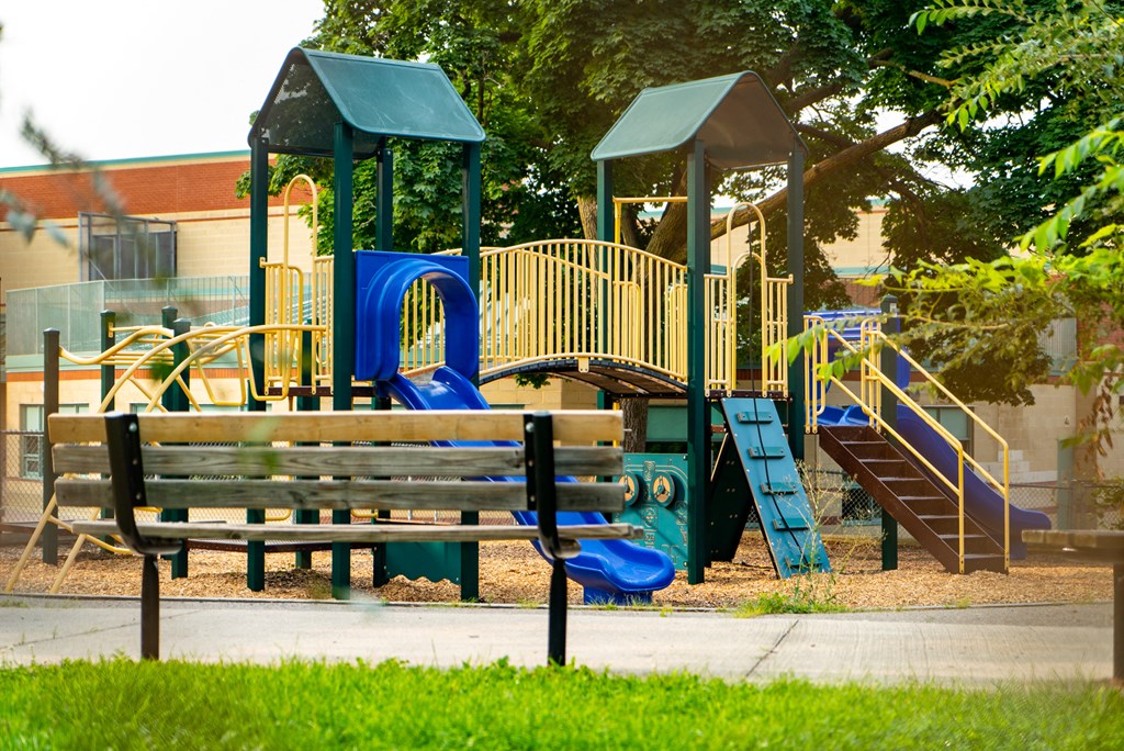a playground with a bench and slides in front of a building