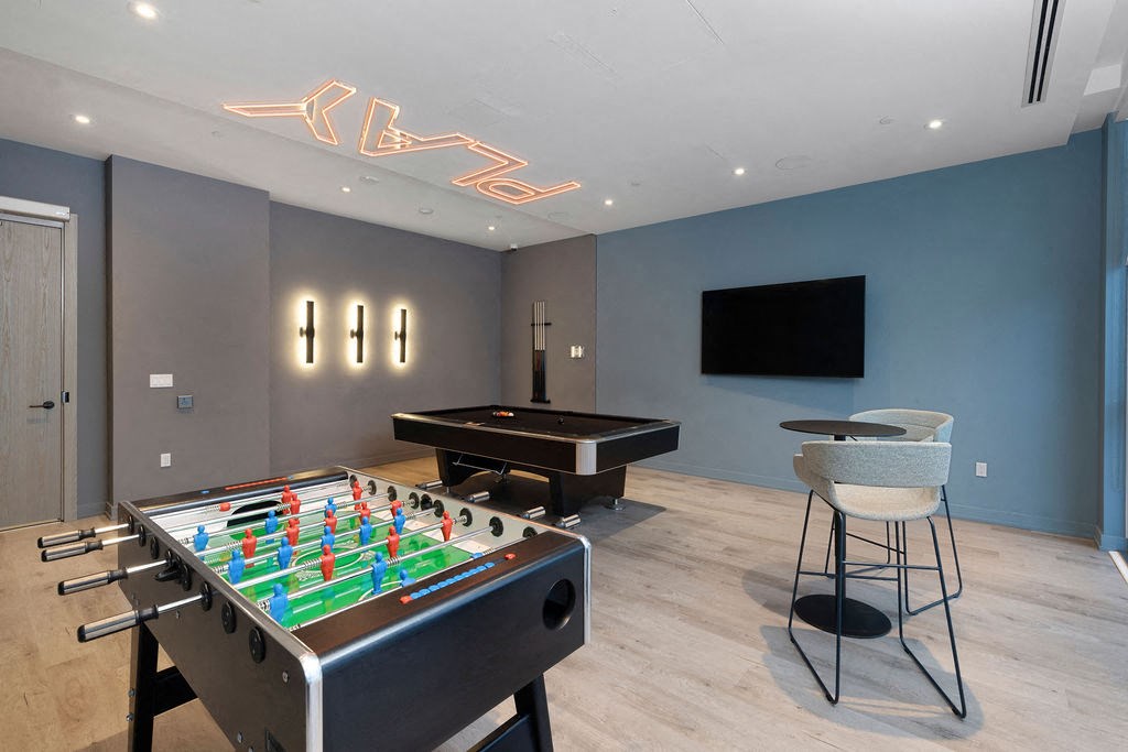 A foosball table is in the middle of a room with a pool table and a chair.