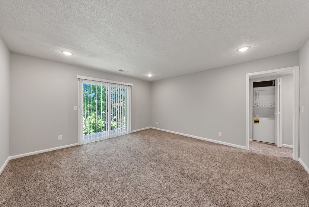 an empty living room with a large window and carpeting