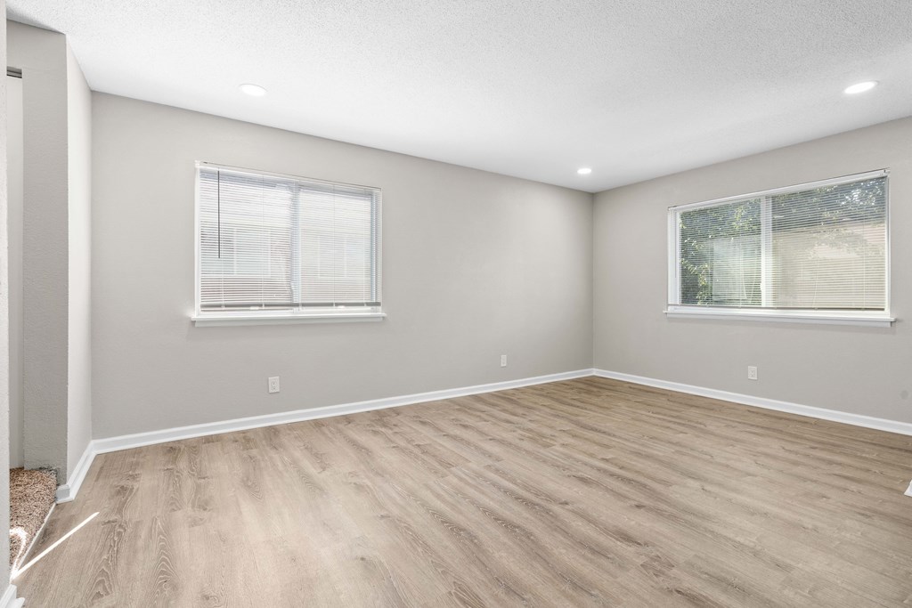 an empty room with wood flooring and two windows