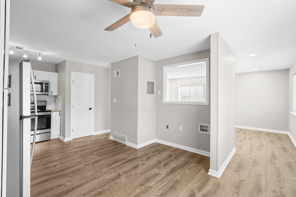 an empty living room with a ceiling fan and a kitchen