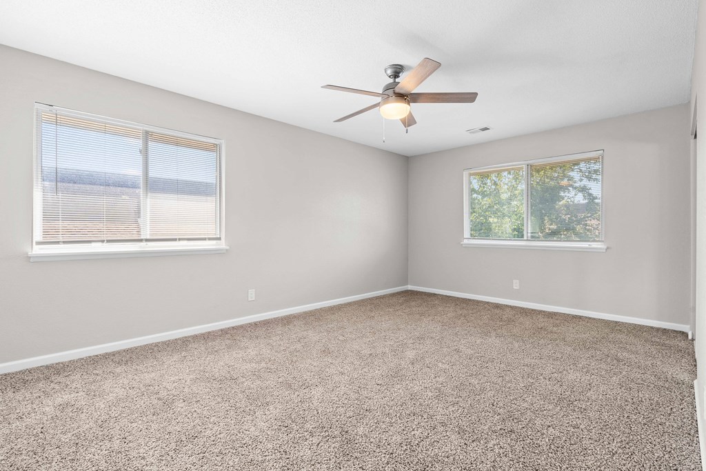 an empty bedroom with a ceiling fan and two windows