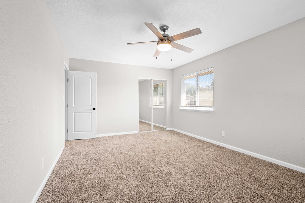 an empty living room with a ceiling fan and a window