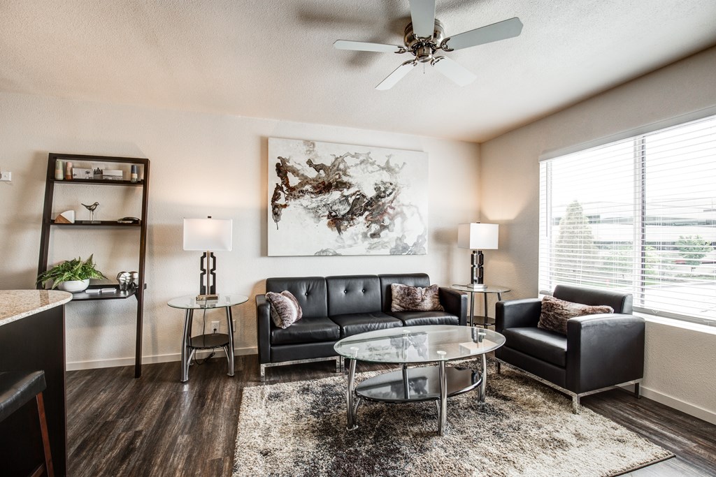A living room with a black couch, a glass coffee table, and a ceiling fan.