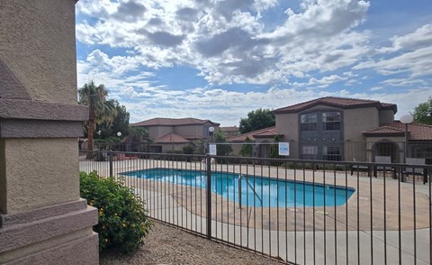 A pool surrounded by a black fence with a house in the background.