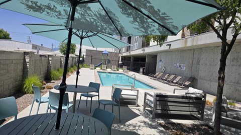 A pool area with a table and chairs under a shade umbrella.