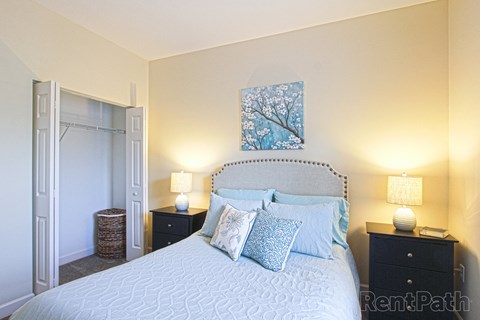 A bedroom with a large bed, two nightstands with lamps, and a painting on the wall.