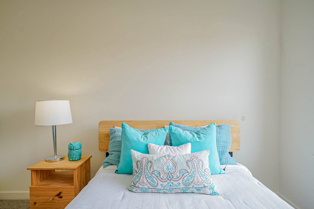 A bed with a white comforter and blue patterned pillow.