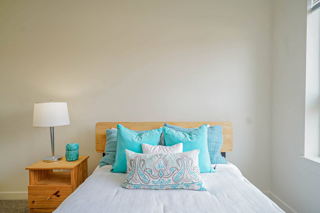 A bed with a white comforter and blue patterned pillow in the middle.