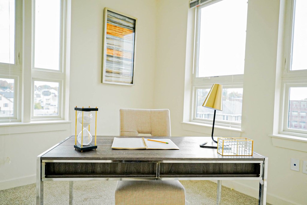 A table with a lamp, a chair, a notebook and a pen on it.