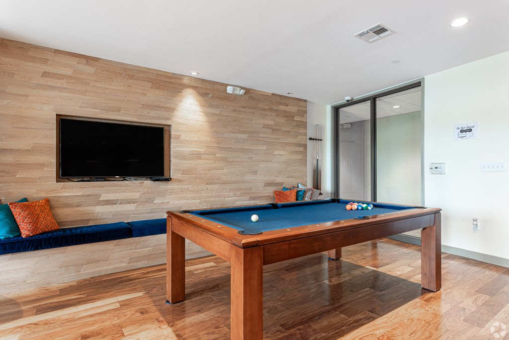 A pool table with a blue cloth and a television on the wall.
