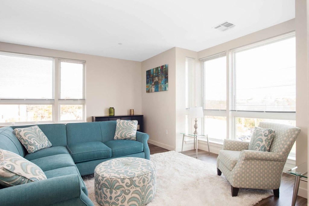A living room with a blue couch and a patterned ottoman.
