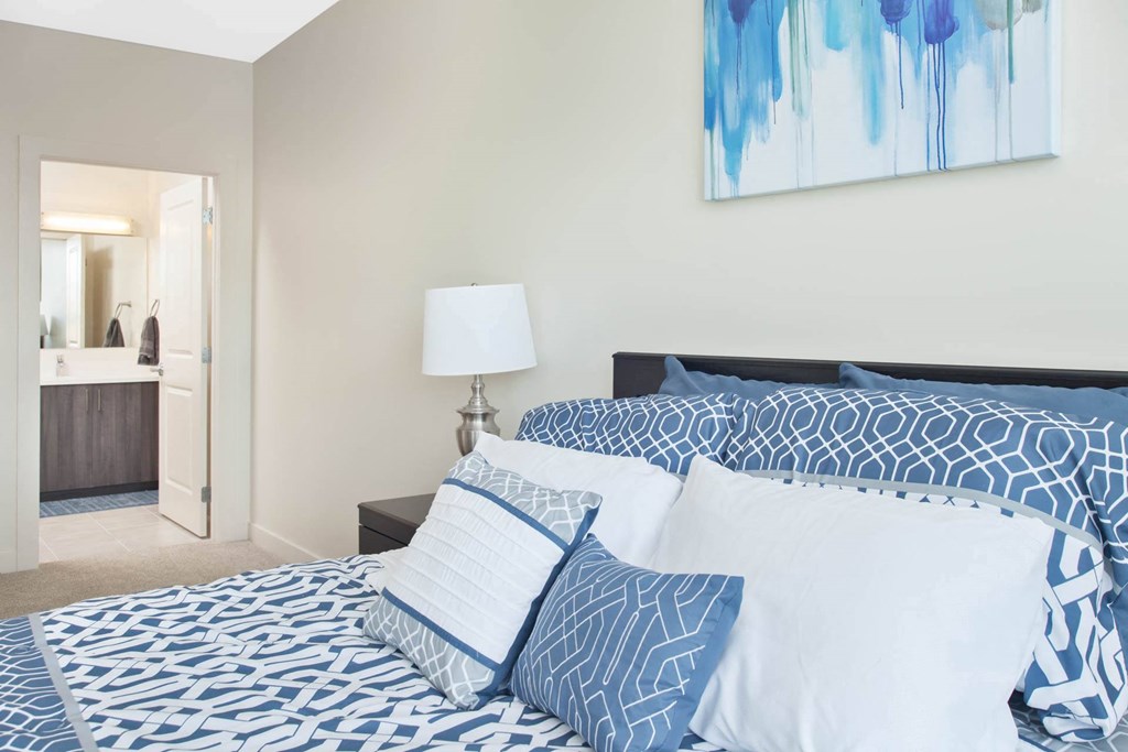 A bed with blue and white bedding and pillows in a room with a painting on the wall.