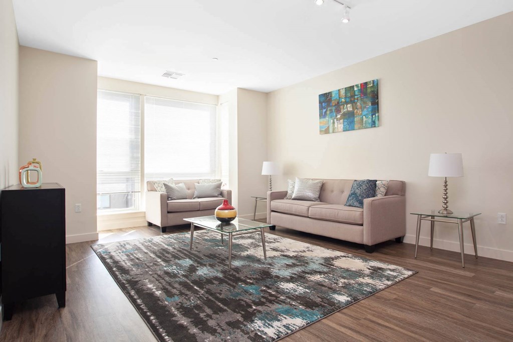 A living room with a rug, a couch, a chair, a table, and a painting on the wall.