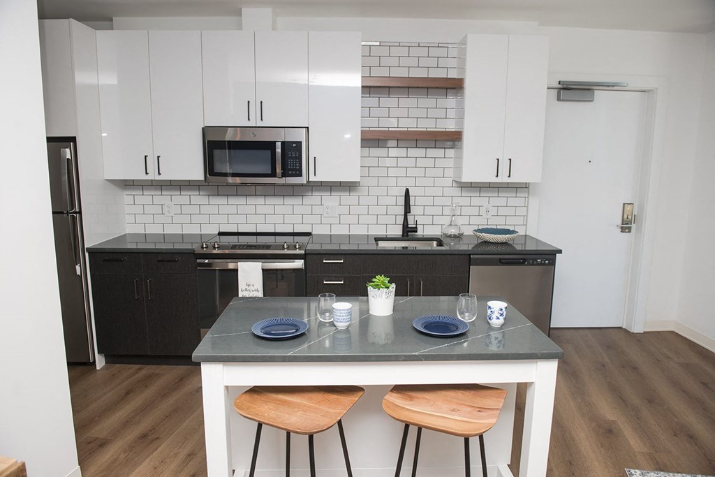 a kitchen with white cabinets and black appliances and a counter with three stools
