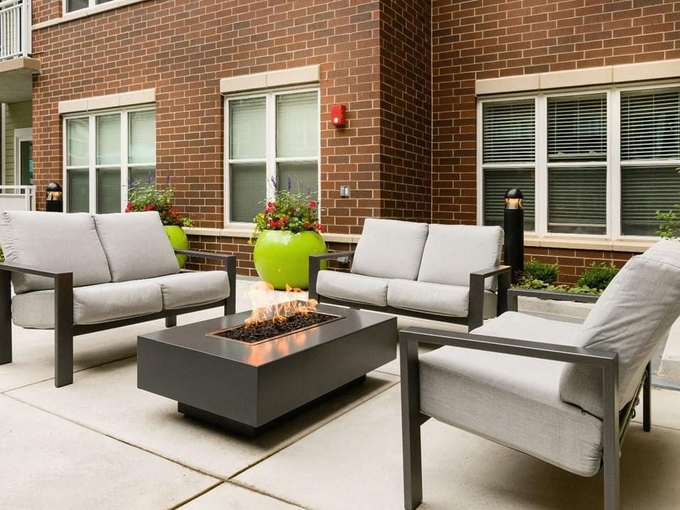 a patio with chairs and a fire pit in front of a brick building