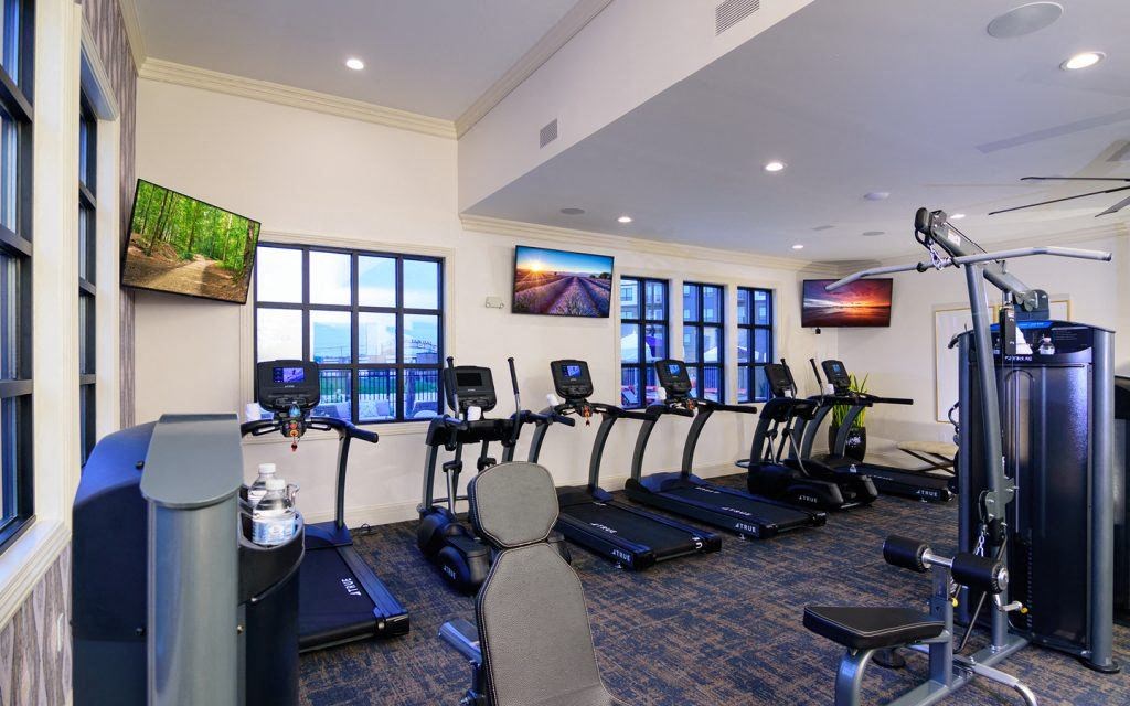 a gym with cardio equipment in a room with windows
