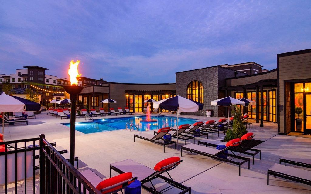 a swimming pool at night with lounge chairs and a fire