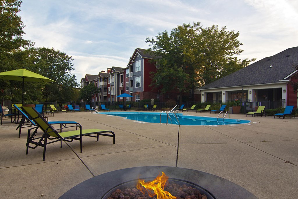 a swimming pool with a fire pit and chairs in front of a poolside house