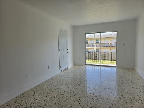 A spacious room with a speckled floor and a view of a balcony through a glass door.
