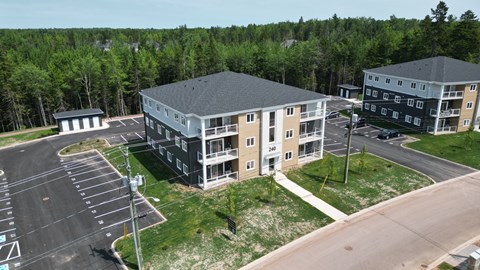 A parking lot in front of a building with a grassy area and trees in the background.