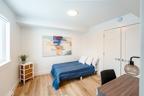 A bedroom with a blue bed and a painting on the wall.