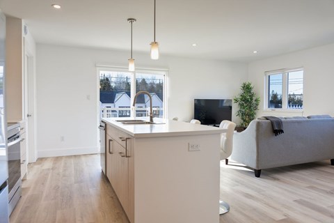 A modern kitchen with a white island and a grey couch in the living room.