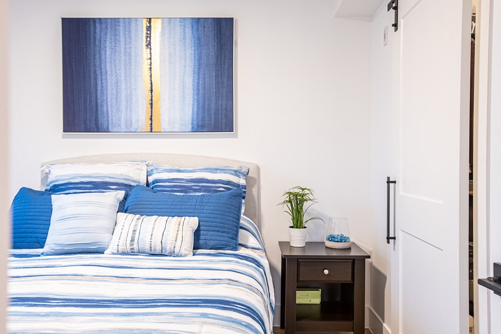 a bedroom with a bed with blue and white pillows and a blue painting above