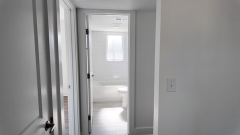 A white hallway with a door on the left and a window on the right.