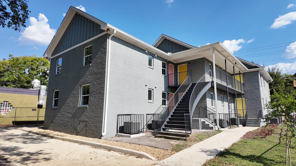 A grey building with a yellow door and a staircase leading to the second floor.