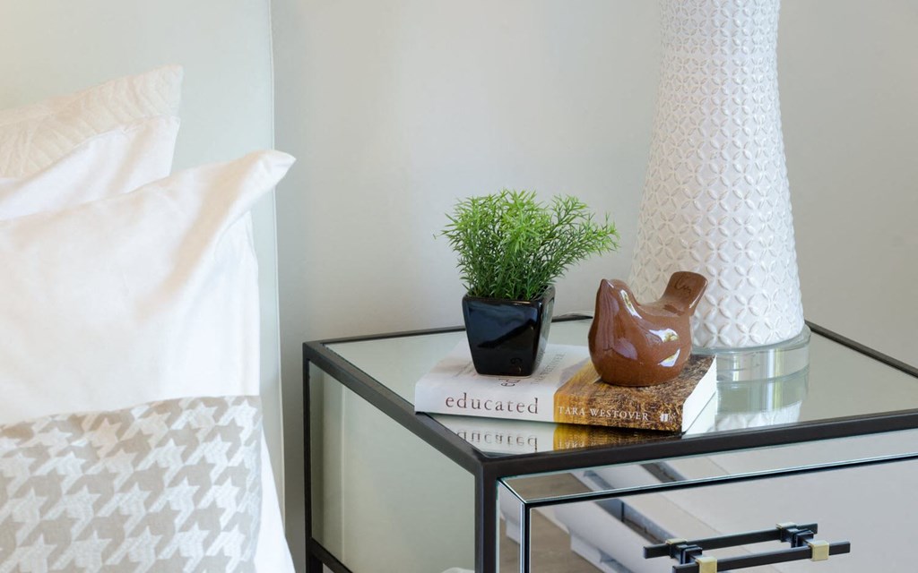 a nightstand with a vase and a book on it next to a bed