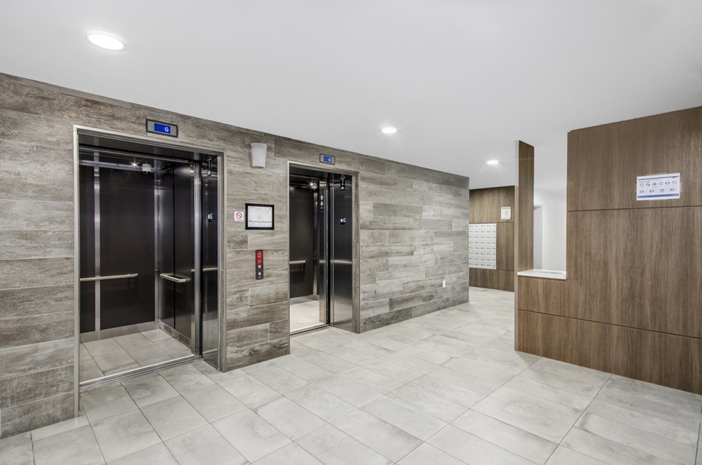 two elevators in the lobby of a building with wood and marble walls and floors