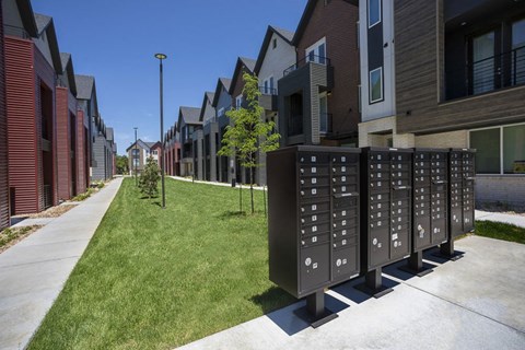 Outdoor view of townhomes with mailboxes and open green space between tow rows of townhomes.