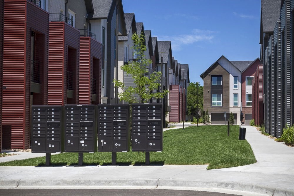 Outdoor view of townhomes with mailboxes and open green space between tow rows of townhomes.