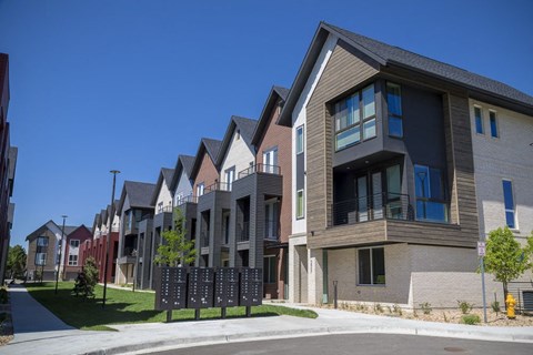 Outdoor view of townhomes with mailboxes and open green space between tow rows of townhomes.