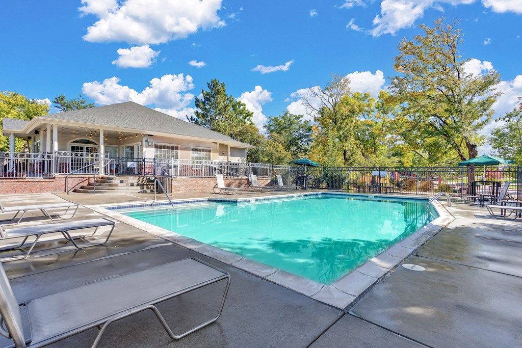 bright blue pool with lawn chairs surrounding the outside and an outside deck overlooking the pool with two bbqs