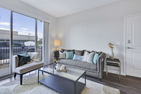 A living room with a grey couch and a glass coffee table.