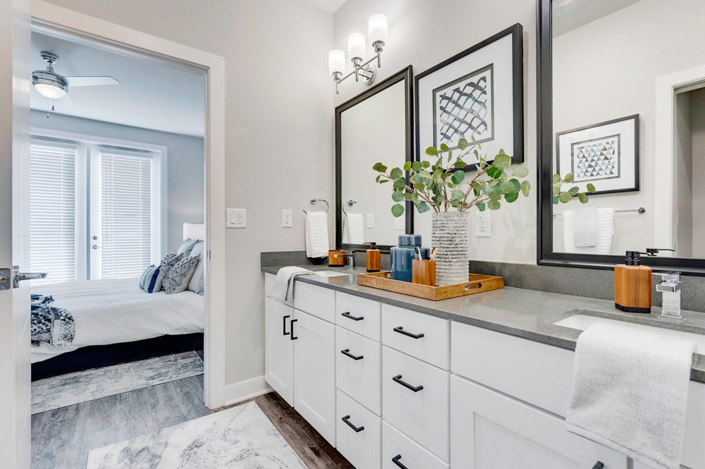Townhome bathroom with dual sinks, large cabinet space, wood floors and entry to the bedroom.