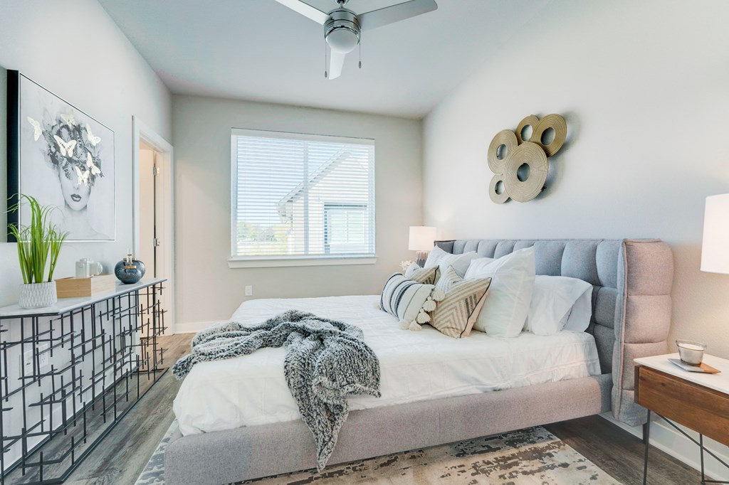Townhome bedroom with wood floors, large bed, ceiling fan and large window.