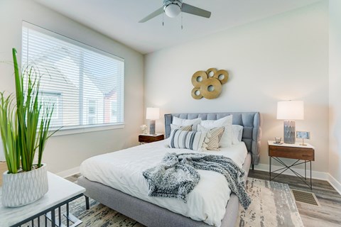 Townhome bedroom with wood floors, large bed, ceiling fan and large window.