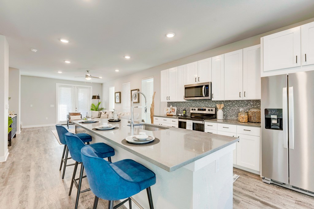 Chef inspired open kitchen with plenty of cabinets and drawers with stainless steel appliances, white cabinetry and quartz countertops