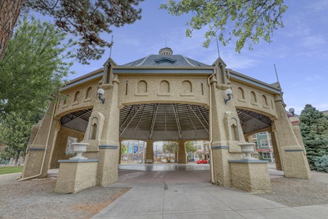 A gazebo-like structure with a dome roof and arched openings is surrounded by trees.