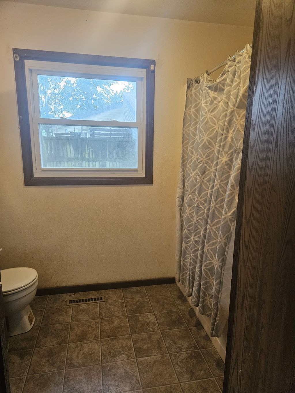 A bathroom with a toilet, a window and a shower curtain.
