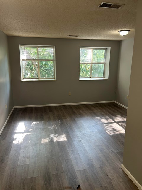 A room with two windows and wood flooring.