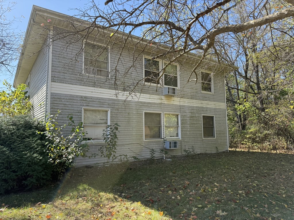 A house with a grey siding and a white trim is surrounded by trees and bushes.